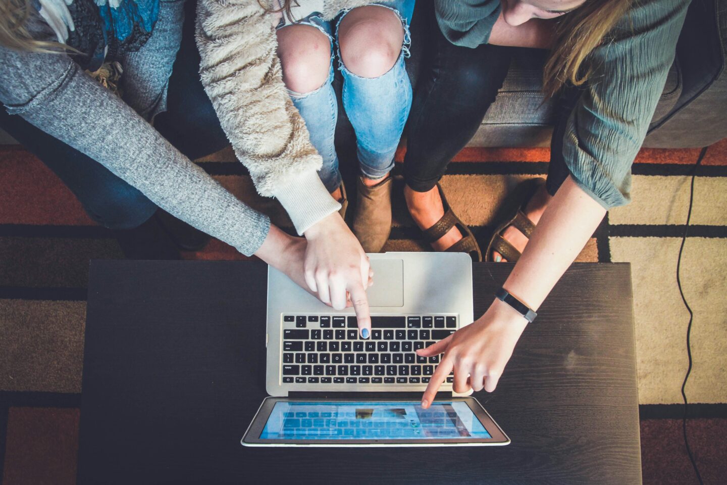 Three people collaborating on a laptop, pointing to the screen while brainstorming ideas in a cozy workspace. A dynamic and creative teamwork atmosphere.