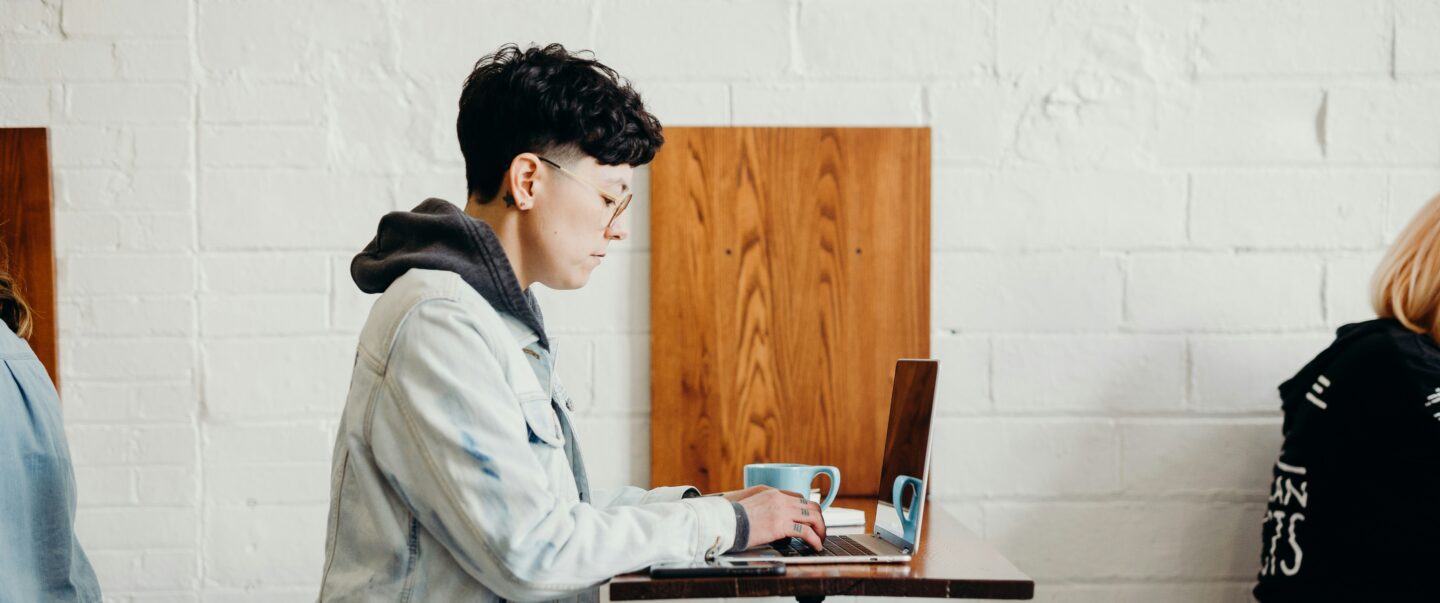 A person seated in a cozy café, focused on their laptop, surrounded by a warm ambiance of coffee cups and a relaxed atmosphere, capturing the essence of productive remote work.