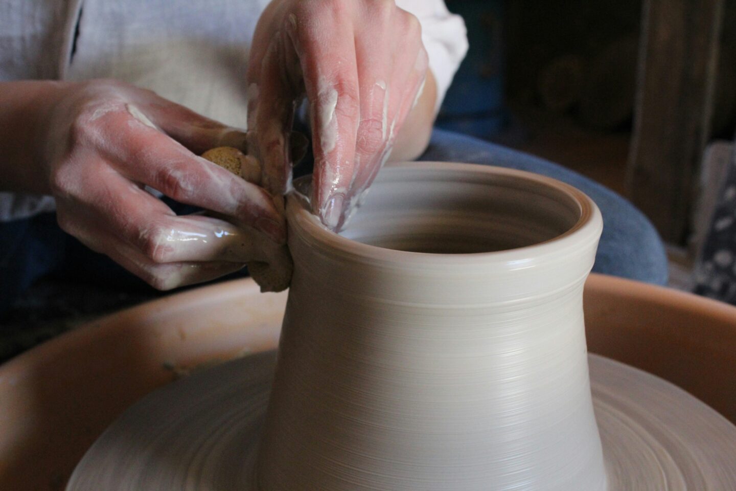 Ceramist crafting a vase in a workshop, surrounded by tools and pottery.