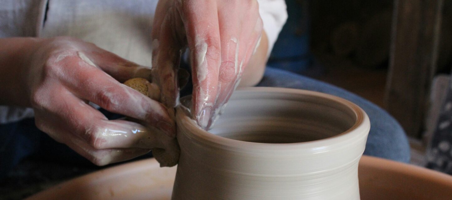 Ceramist crafting a vase in a workshop, surrounded by tools and pottery.